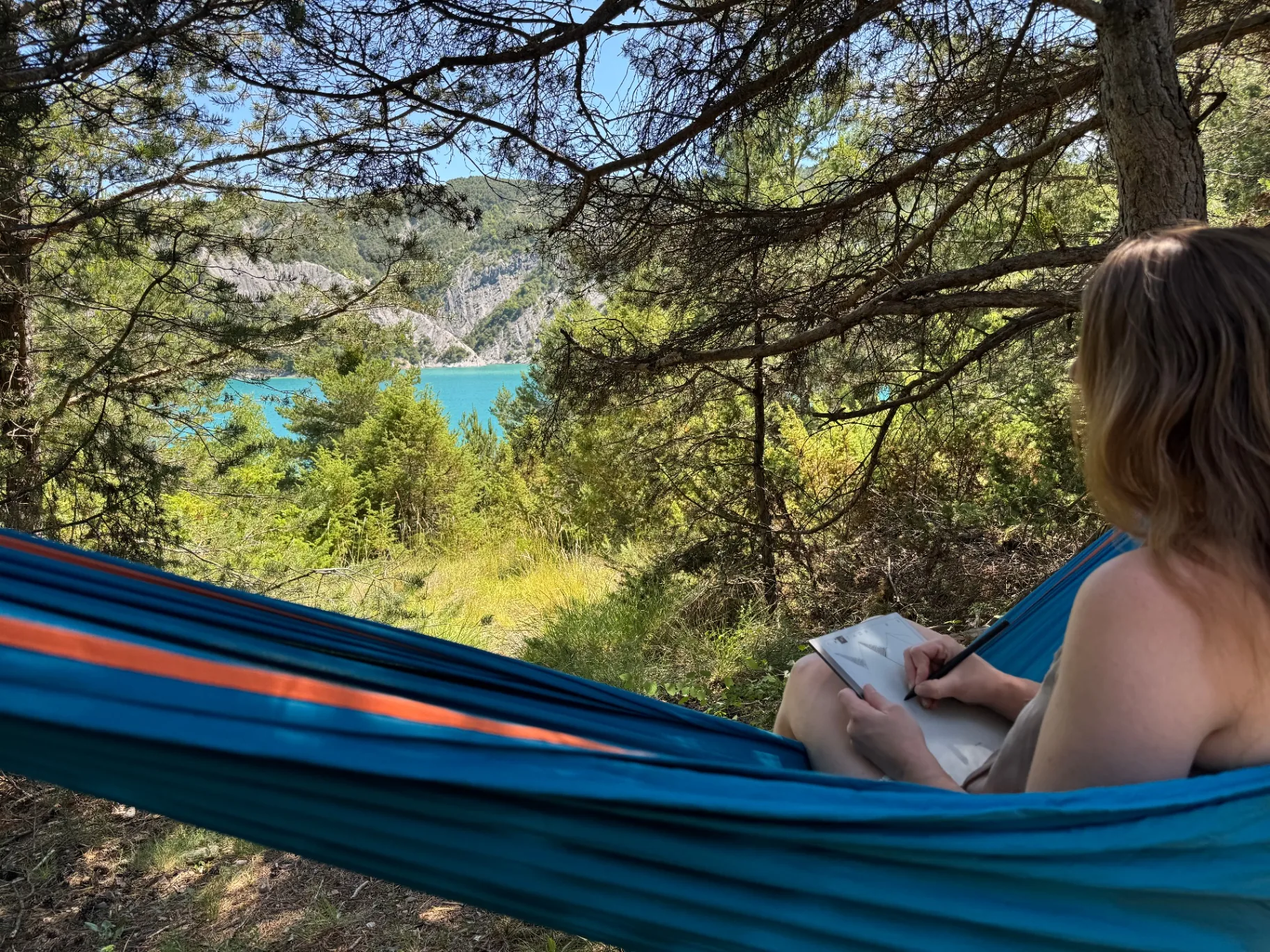Clémence dessinant depuis un hamac au-dessus du Lac de Serre-Ponçon — artiste des Alpes françaises au travail