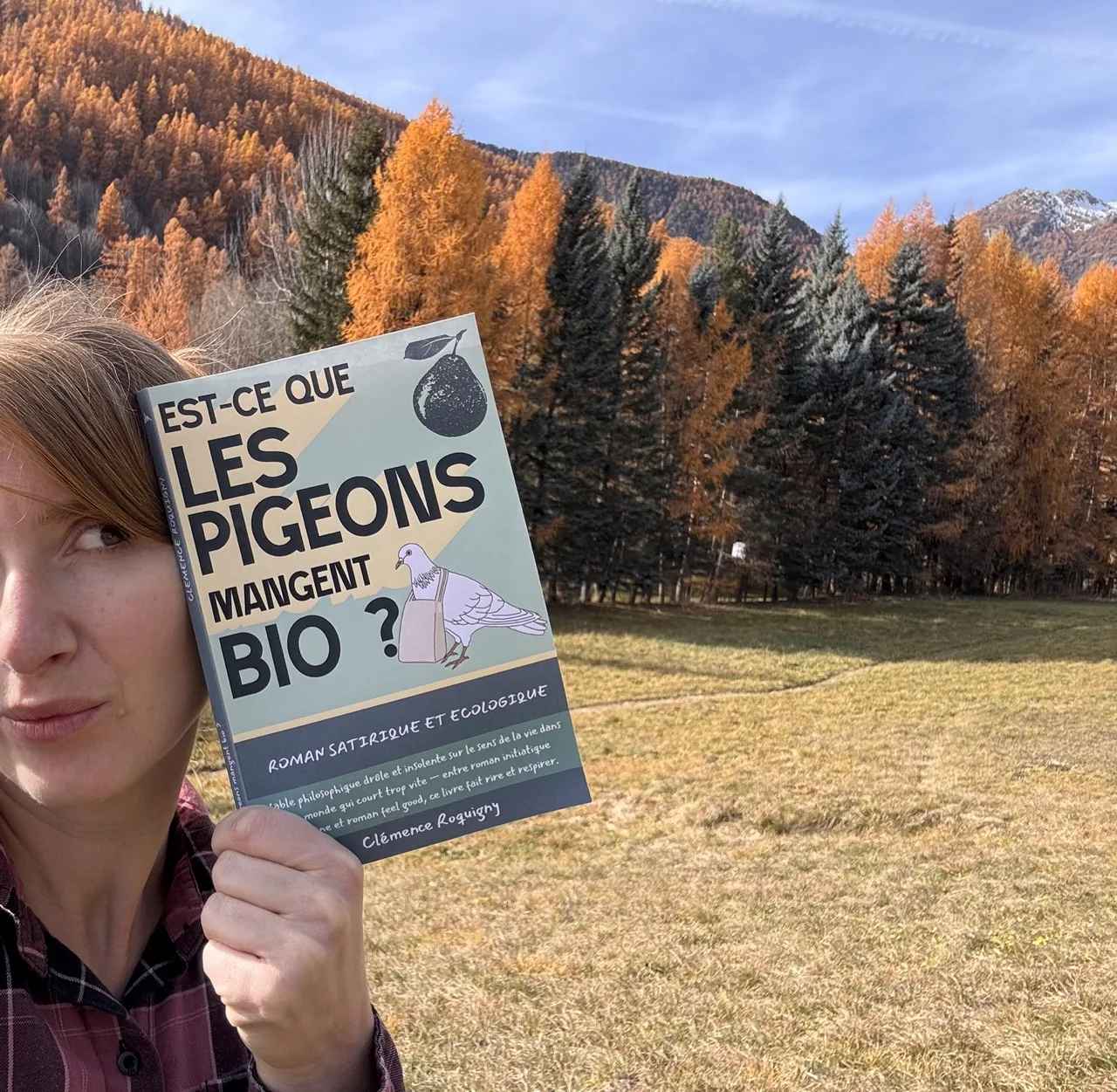Clémence tenant son roman dans les mélèzes d'automne de la vallée de Serre Chevalier